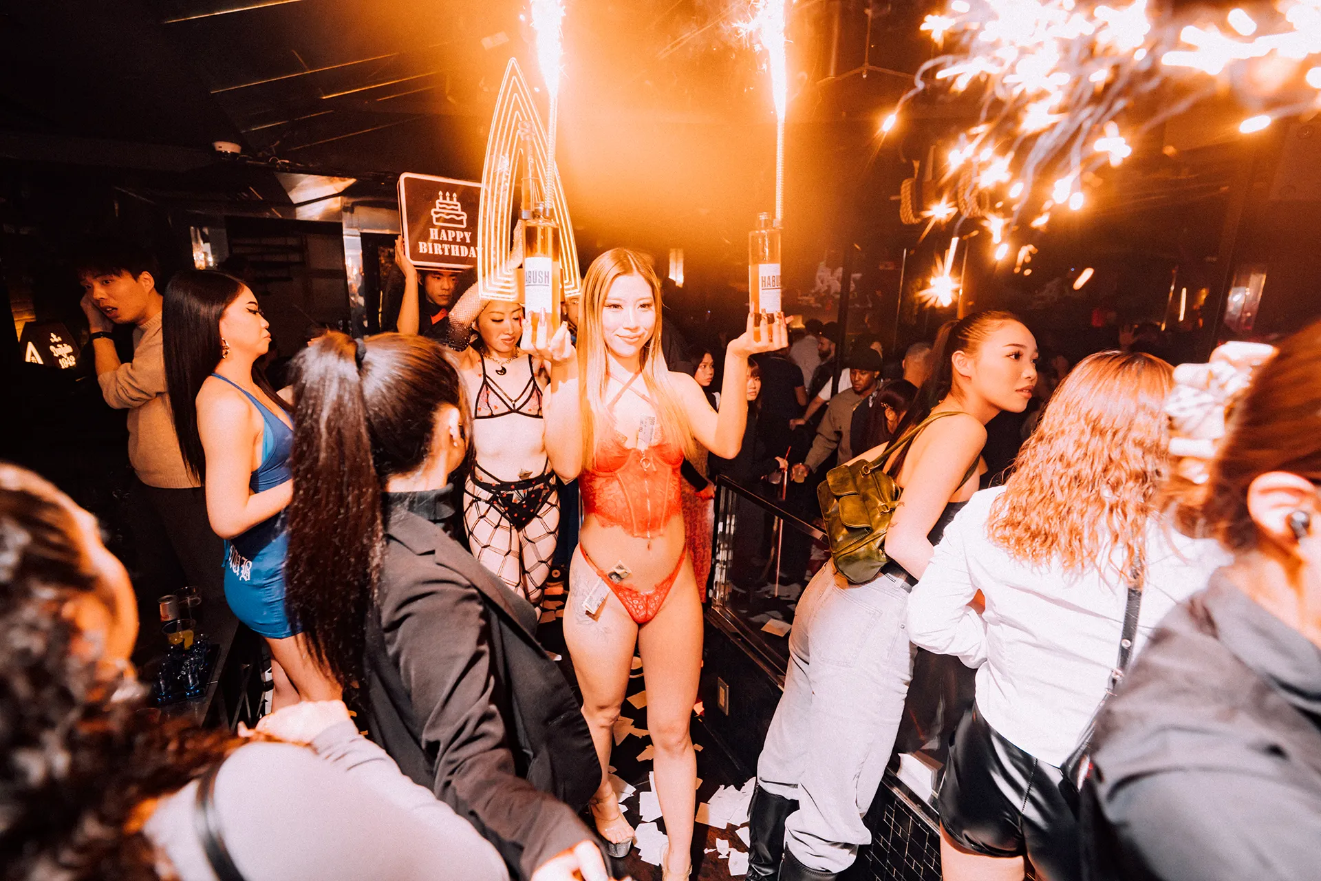 Staff carrying sparkler bottles through the crowd with a Happy Birthday sign at GALA RESORT